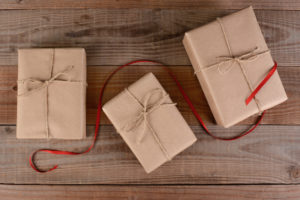 High angle shot of three plain wrapped Christmas presents. Brown paper and twine wrapped packages with a red ribbon running through the middle on rustic wood surface.